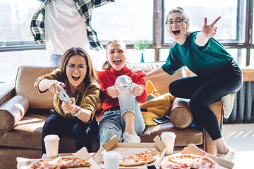 Group of young people screaming celebrating victory while playing game pad and eating pizza © BullRun