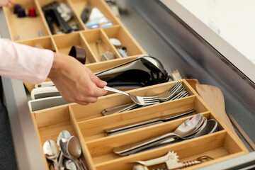 Woman organizing clean cutlery and kitchenware in kitchen drawer, tidying up cutlery tray, closeup