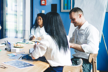 Obraz premium Considerate multiethnic colleagues discussing graphs while sitting in office