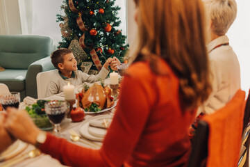 Family holding hands saying grace at christmas dinner table