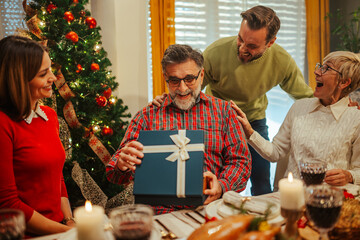 Family celebrating christmas giving present to grandfather