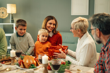 Family giving christmas present to grandmother at dinner table