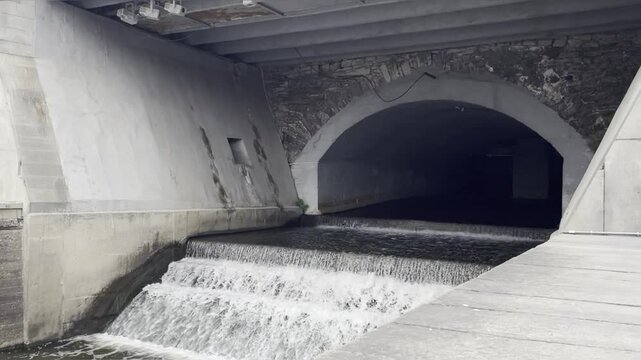 Small grey concrete dam in the city with waterfall moving into river