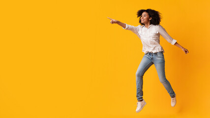 Look there. Excited Afro Woman Jumping And Pointing Aside At Copy Space On Yellow Background, Full-Lenght