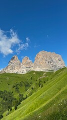 Scenic Mountain Landscape Under Clear Blue Sky in Dolomites, Italy. Breathtaking view of towering italien mountains with lush green slopes under a bright blue sky