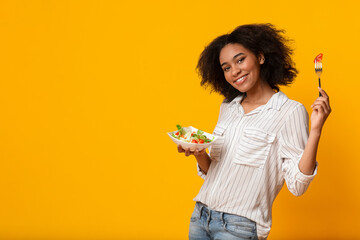 Tasty Dieting. Cheerful African American Girl Eating Fresh Vegetable Salad And Posing At Camera In Studio Over Yellow Background, Copy Space