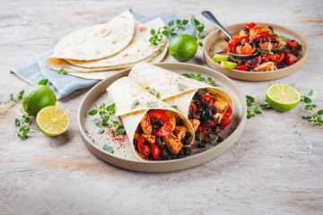 Mexican style burritos - tortilla wrap with spicy chicken meat breast filet nuggets, vegetables and black olives served as closeup with hot spices on a design plate