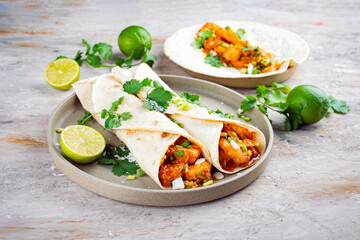 Caribbean style wrap with king prawns in spicy coconut curry lime salsa served as closeup in a wheat tortilla on a design plate