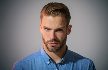Obraz premium Portrait of serious man in casual wear with trendy hairstyle. Fashionable male with beard and mustache. Sexy male model in denim shirt with stylish hairdo. Advertising for barbershop. Fashion for men.