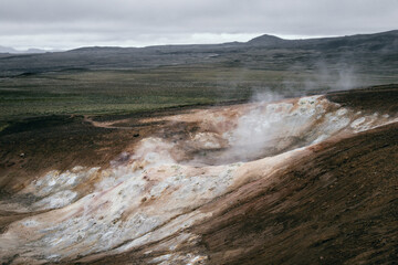 An open vulcanic area in Iceland with a steaming crator in different colors from white to brown