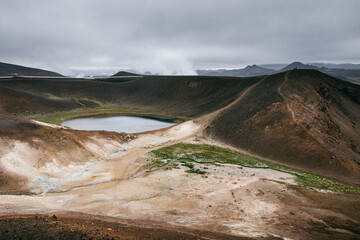 An old crator with a small lake and active geothermal activity in Iceland, in the background an geothermal energy is used 