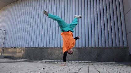 young energetic guy dancer breaksdancing outdoors in the city on the street against the background of a wall, a male acrobat doing extreme tricks and dancing hip-hop