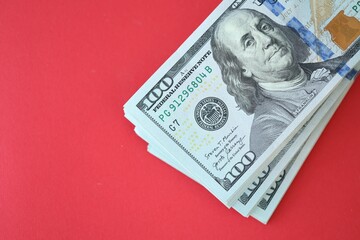 Big amount of hundred dollar bills in thick stack lies on bright red color paper background