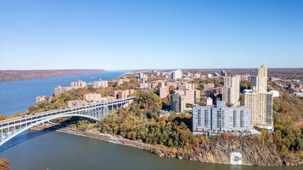 Fototapeta premium This location in the Bronx offers stunning views of lush greenery, a picturesque lake, and urban structures. Framed by the river, it showcases iconic bridges and the New York City skyline in the dista