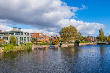 Obraz premium A scenic view of a lush garden and traditional brick houses by the water on the Northern Amstel Canal, surrounded by autumn foliage and clear blue sky reflections. Amsterdam, the Netherlands.