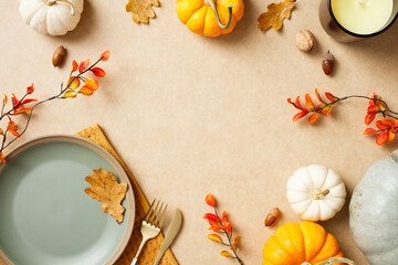 Autumn flat lay with empty ceramic plate, pumpkins, leaves, berries, and a candle on a neutral background.