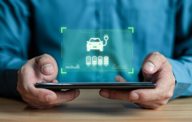 Businessman using Mobile phone displaying Electric Car EV battery charging station charging in car port 