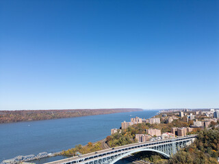 Obraz premium This location in the Bronx offers stunning views of lush greenery, a picturesque lake, and urban structures. Framed by the river, it showcases iconic bridges and the New York City skyline 