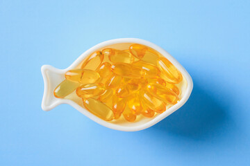 Golden omega-3 capsules in a fish-shaped dish on a blue background.