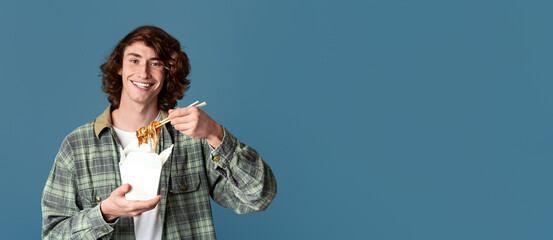 Takeaway food. Happy millennial guy eating chinese noodles from disposable box, turquoise...