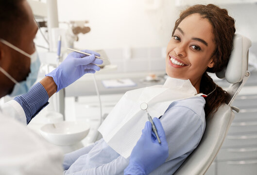 Pretty black happy woman in dentist chair ready for regular check up in modern stomatological clinic