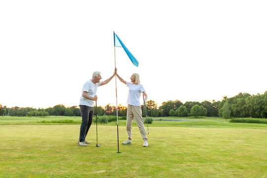 elderly senior couple in uniform celebrating victory and success in golf game and giving high five, old man and woman playing golf on golf course at sunset and doing outdoor sports