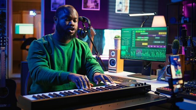 Artist songwriter hosting online master class to teach piano lessons on internet vlog, electronic keyboard notes in home studio. Young composer playing on synthesizer, recording video. Camera B.