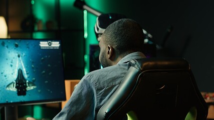 African american player in neon illuminated apartment paying close attention to computer screen during videogame competitive match. Person competing in internet esports tournament, camera A