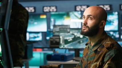 Military soldier in mission control center overseeing national safety operations with devices, close up. Middle Eastern army specialist examining data in monitoring room command center, camera A