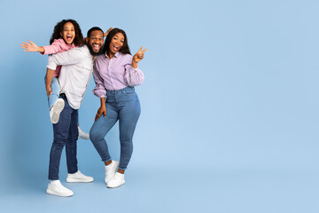 Spending Time With Family Is Fun. Full body length of excited African American man, woman and girl laughing and posing isolated over yellow studio wall. Cheerful father carrying his daughter on back