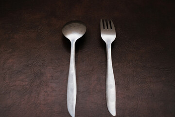 Fork and spoon stainless isolated on brown background, top view, eating place setting.