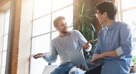 Two young multiracial coworkers having conversation during break time in office, copy space