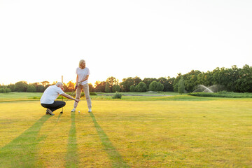 old man and woman in uniform playing golf on golf course at sunset, elderly couple having active outdoor recreation and doing sports, grandpa and grandma holding clubs and pointing where to hit the
