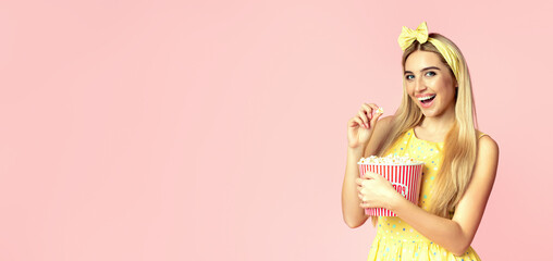 Watching Movie. Cheerful beautiful blonde girl eating popcorn isolated over pink studio wall, copyspace