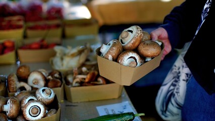 hand of an elderly woman holding a paper box with mushrooms at a farmer's market
