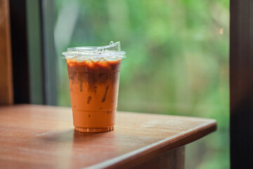 Glass of iced milk tea with coffee on woodden. table in coffee shop.