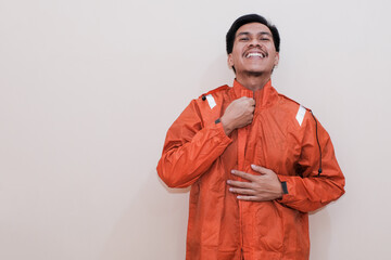 Smiling Southeast Asian man wearing orange raincoat with hands for zip up them looking at the camera. Positive person. standing over isolated white background. rainy season.