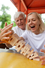 elderly senior couple playing board game and building a tower with wooden bricks outdoors in the...