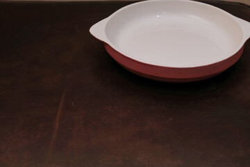 Empty white ceramic plate with grey on the down and handle on the side isolated on brown background, eating place setting.