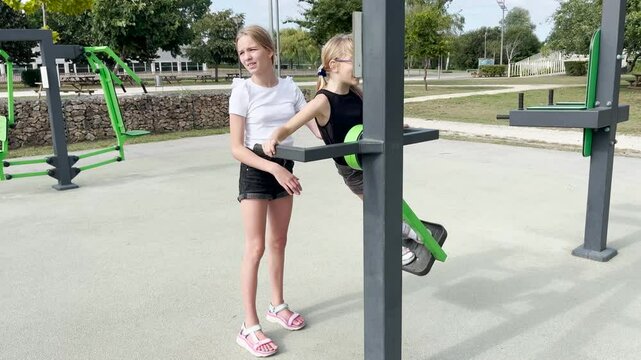 Two sisters play sports. It is summer on the street and children are playing on the sports playground outside.