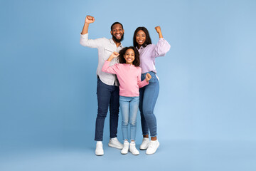 Yes. Full body length of excited young black family of three people shaking clenched fists, making...