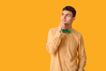 Thoughtful young man with green stylish bow tie on yellow background