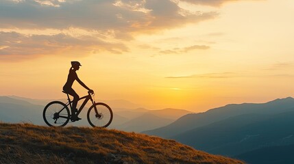 Silhouette of a cyclist on a hilltop during sunset with mountains in the background.