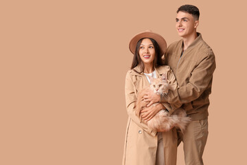 Beautiful young couple with cute Maine Coon cat on brown background
