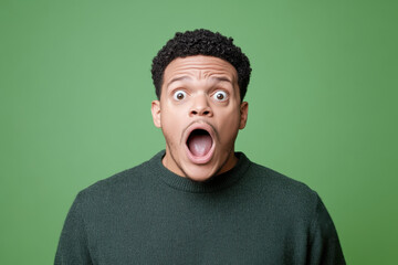 Shocked expression on man with curly hair against green background, conveying surprise and disbelief. His wide open mouth and eyes reflect strong emotional reaction