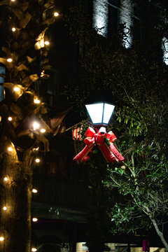 A street lamp decorated for Christmas with a red and gold bow, green garland, and yellow Christmas lights at night in downtown Savannah, GA