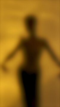 Vertical 4K video. Blurred background. Woman in skirt dances out of focus on golden yellow wave background. Dark silhouette of unrecognizable people. Concept of beauty, fashion, fantasy, luxury, dream