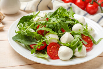 Tasty salad with arugula, spinach, mozzarella cheese and tomatoes on wooden table, closeup
