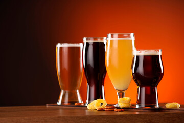 Glasses with different types of beer on wooden table against color background