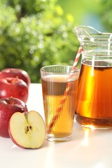 Tasty apple juice in glass, jug and fresh fruits on white table outdoors